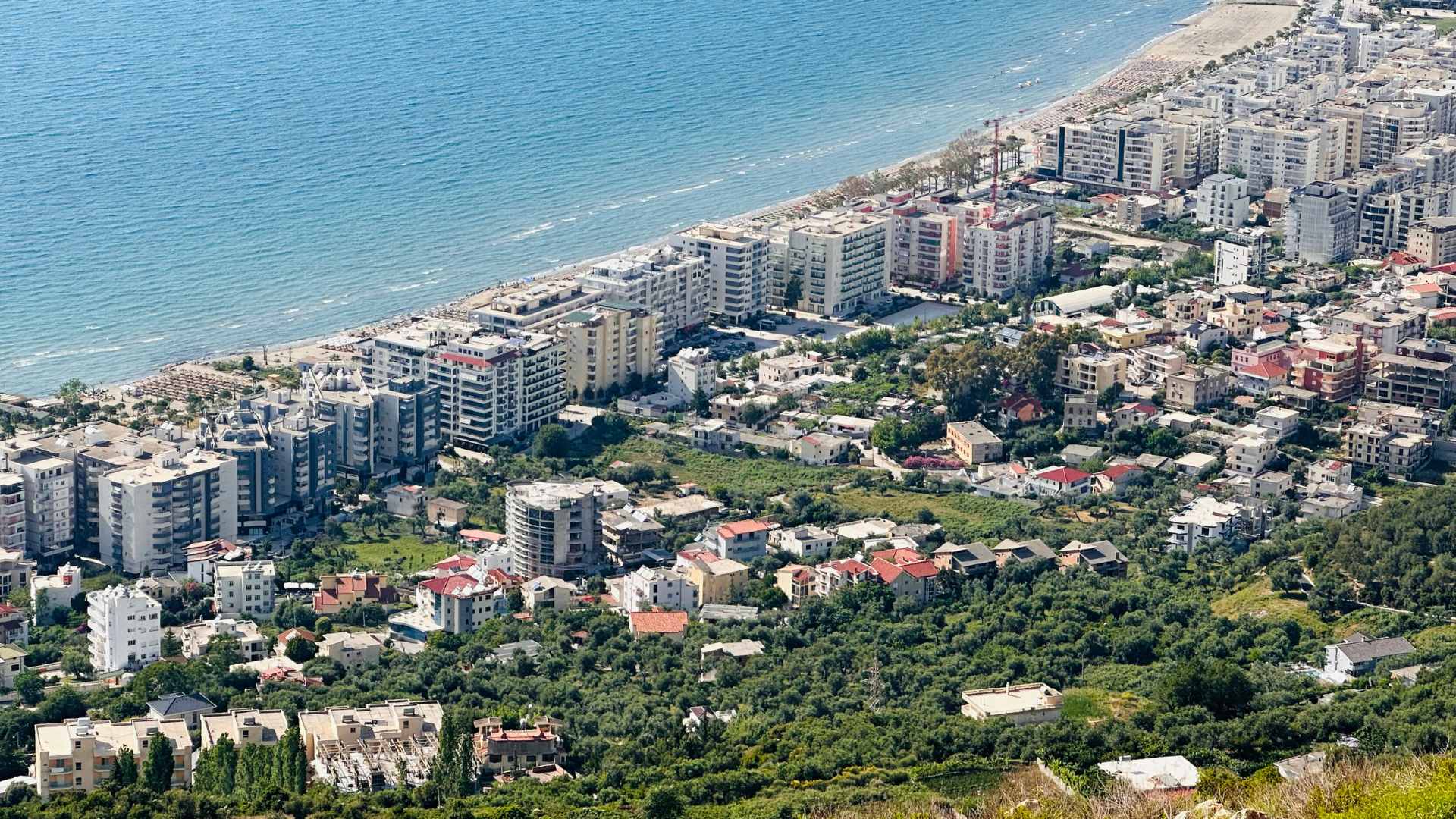 Aerial view of an Albanian coastal city: apartment blocks along a long sandy beach and turquoise sea